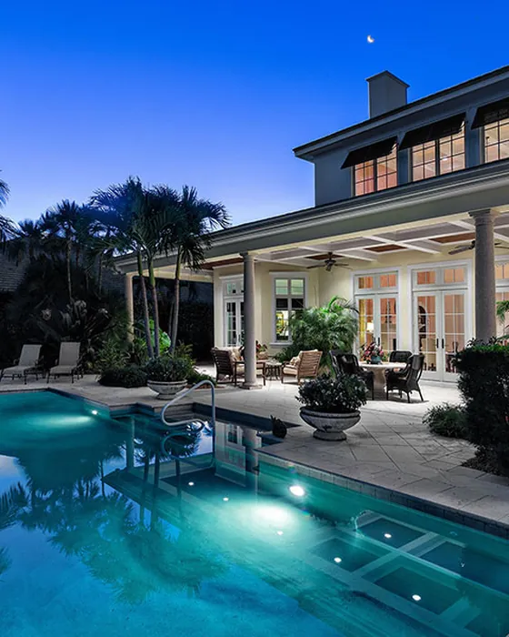 Luxury South Florida home exterior at dusk with a lit pool and covered patio